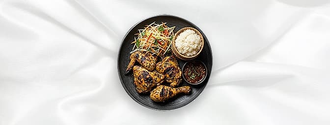 Gai Yang — Thai style barbecued chicken with Thai herbs and spices served with a spicy dipping sauce, sticky rice and Som Tum
