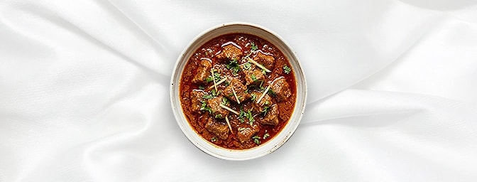 Rogan Josh Kashmiri — A legendary Kashmiri classic. Tender lamb is slow-cooked in a vibrant, jewel-toned sauce seasoned with